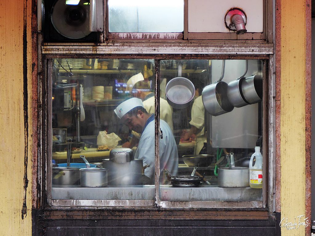 A cook makes ramen noodles in a kitchen packed with pans and dishes, Fukuoka Japan